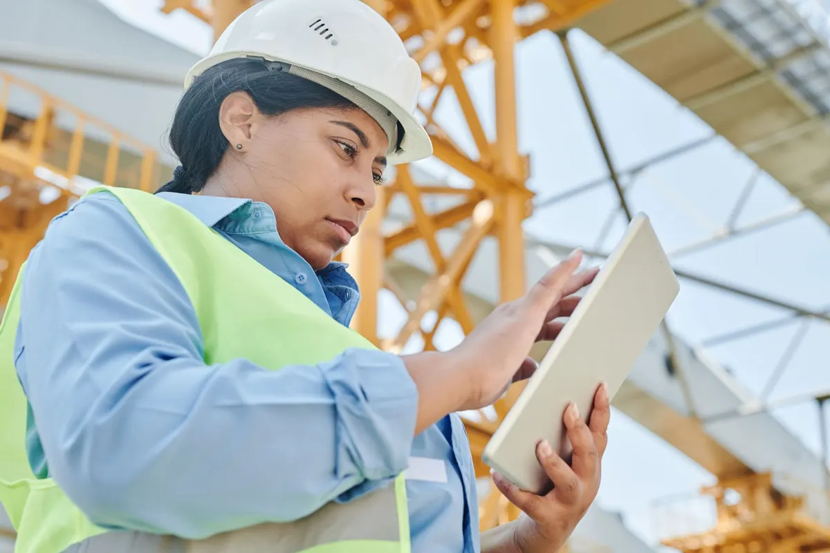 A site engineer in hi-vis and a hard hat using a tablet on site